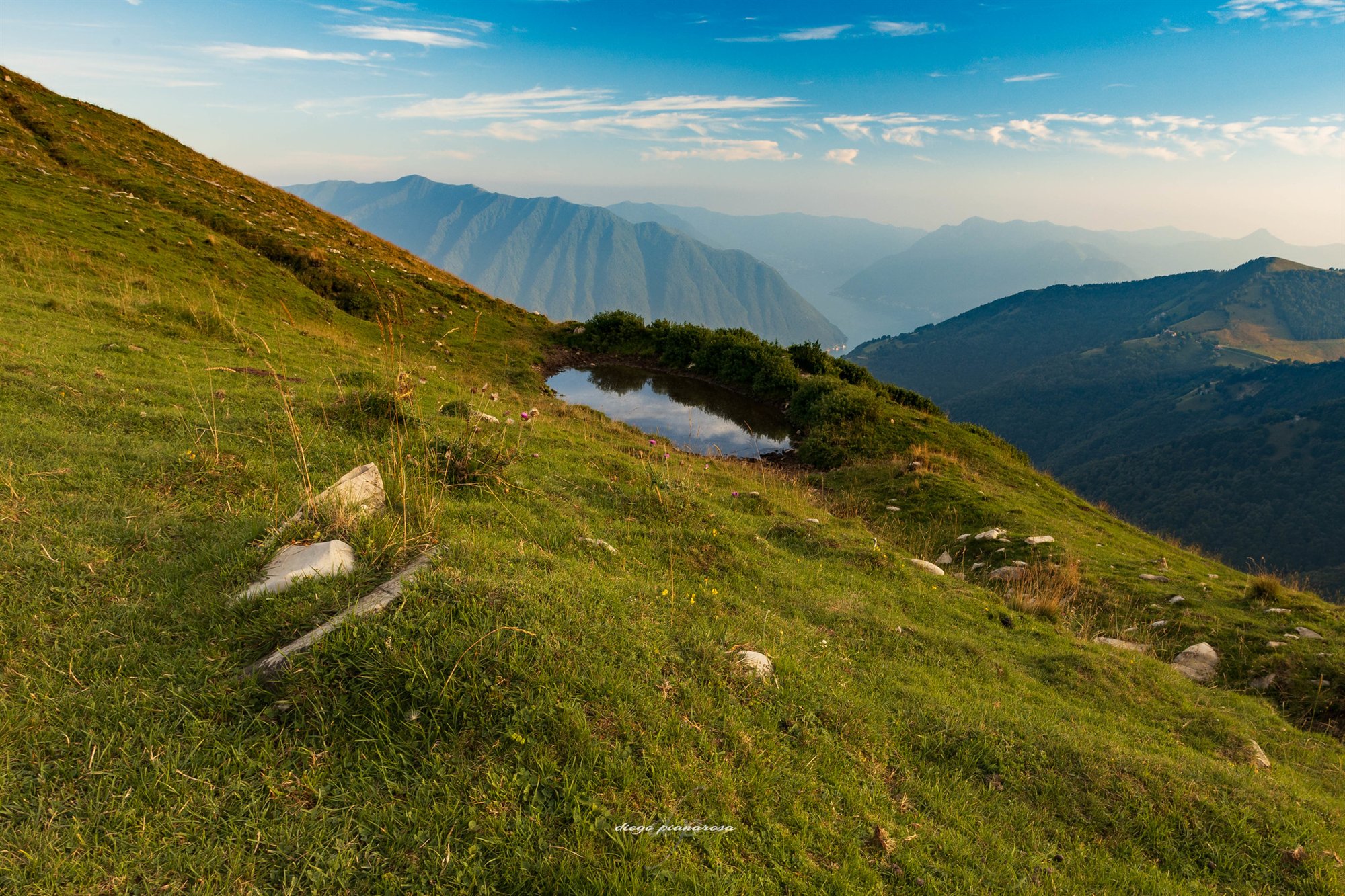 Pendio erboso che scende verso un lago fra le montagne nella foschia