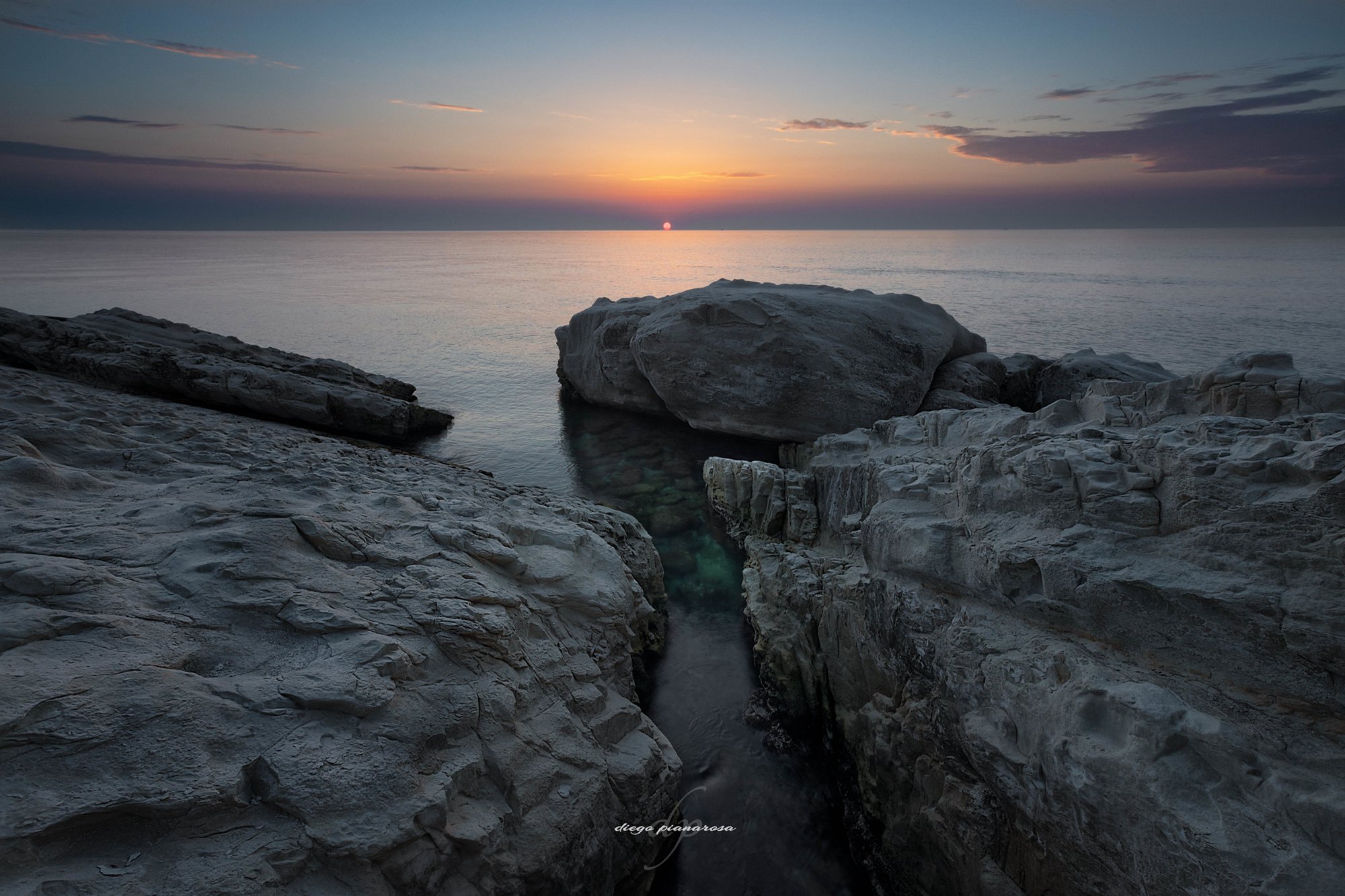 Alba sul mare vista attraverso una spaccatura fra scogli chiari
